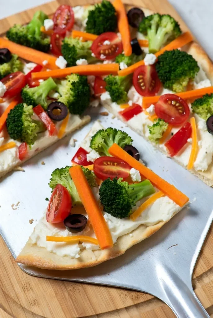 Close-up of vibrant savory vegetable pizza slices with cream cheese, broccoli, tomatoes, carrots, olives, and cheeses.